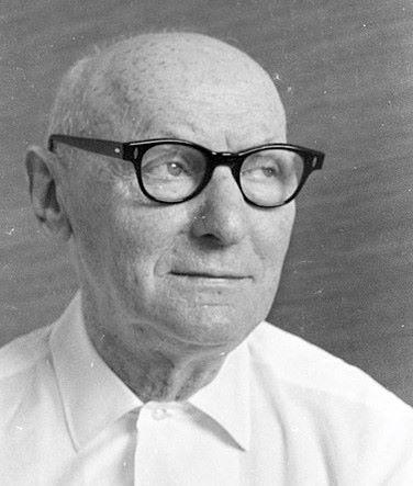 Bald man wearing thick black glasses and white collared shirt