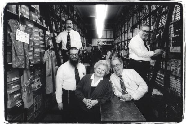 Black and white photo of employees inside menswear storeroom. 