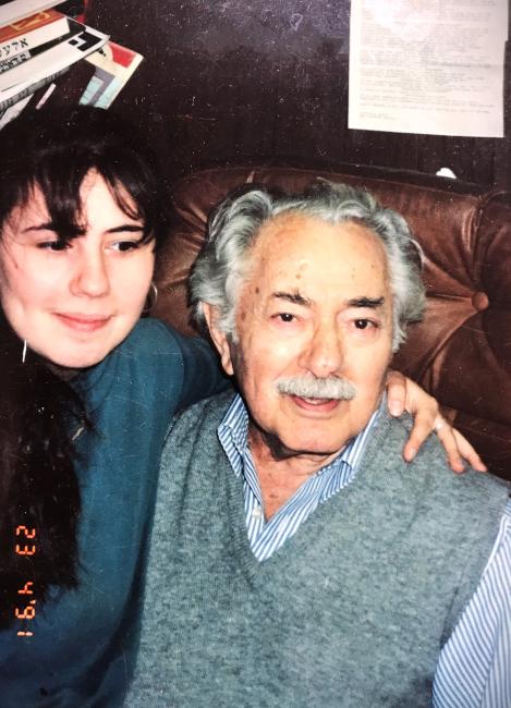 An old white man wearing a grey sweater poses with a young white woman with long black hair, wearing a blue sweater