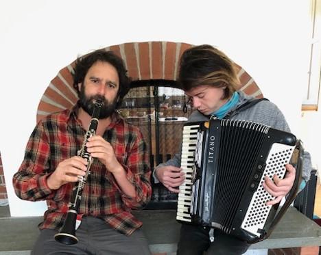 A clarinetist and an accordion player sit and play on a bench. 